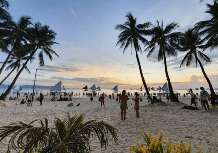 Boracay White Beach with palm trees and tourists during sunset with sailboats in Boracay Philippines