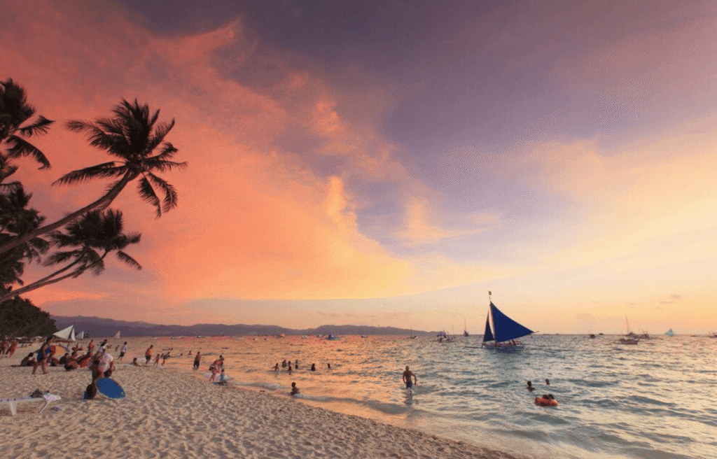 Boracay sunset beach with palm trees, tourists, and paraw sailboat on White Beach Boracay Philippines